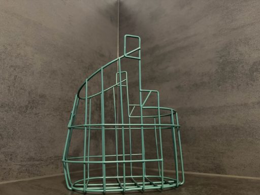 Drahtgestell in Form einer geometrischen Treppe vor einer grauen Wand.